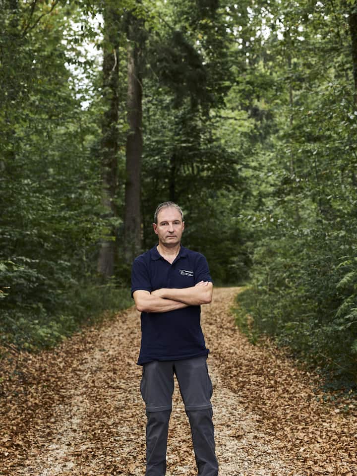 Kantonsförster Rolf Manser steht auf einem Waldweg umgeben von braunem Laub.