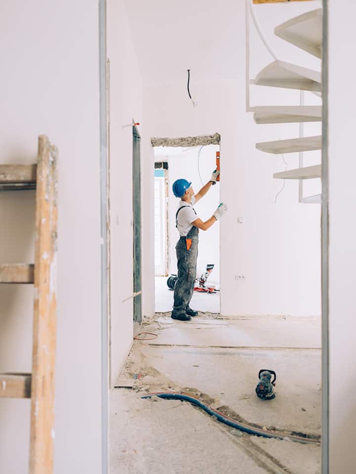 A construction worker wearing a blue helmet using a leveling tool for walls inside an apartment.