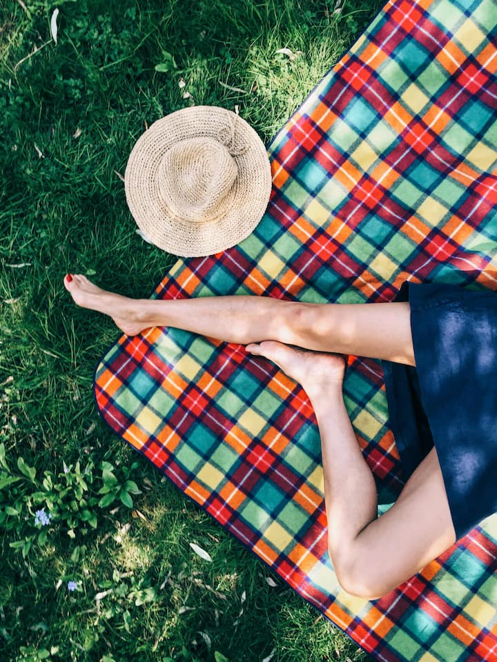 So kommen auch Bewegungsmuffel auf Trab Farbige Picknick-Decke auf einer Wiese mit nackten Beinen einer Person. Bewegungsmuffel stehen schnell unter Verdacht: zu bequem, zu undiszipliniert, zu wenig Willenskraft. Dabei tut ihr Körper genau das, wofür er gemacht ist: Energie sparen. Wie man sich trotzdem mehr bewegt.
