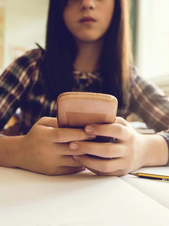 Close up of elementary student typing text message on smart phone while sitting at the desk in the classroom.
639440474