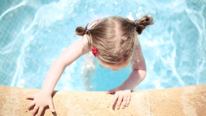 Wenn Kinder ausserhalb vom Wasser ertrinken Ein Mädchen hält sich am Rande des Schwimmbeckens fest aus der Vogelperspektive. Auch Beinahe-Badeunfälle können tödlich enden. Das nennt sich dann sekundäres Ertrinken.