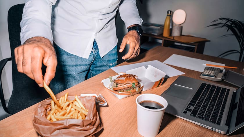 Ist schon wieder Schluss mit Homeoffice? Männerhand mit Pommes im Homeoffice vor dem Computer