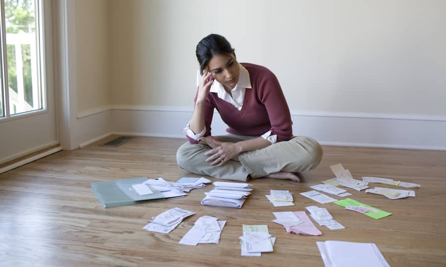Eine junge Frau sitzt auf dem Fussboden und um sich herum hat sie eine Menge Quittungen und Belege ausgebreitet.