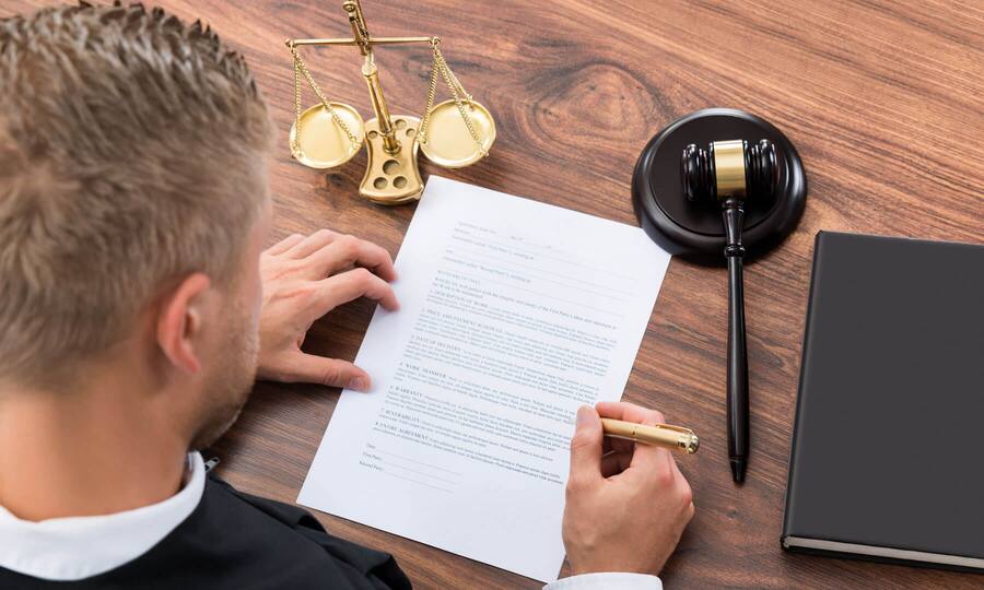 Ein Mann füllt ein Formular aus, das neben einem Richterhammer und einer Waagschale für Gerechtigkeit liegt. In welchen Fällen lohnt es sich, Einsprache gegen einen Strafbefehl zu erheben?