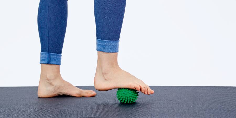 Eine Frau rollt einen genoppten Ball unter ihrer Fusssohle.