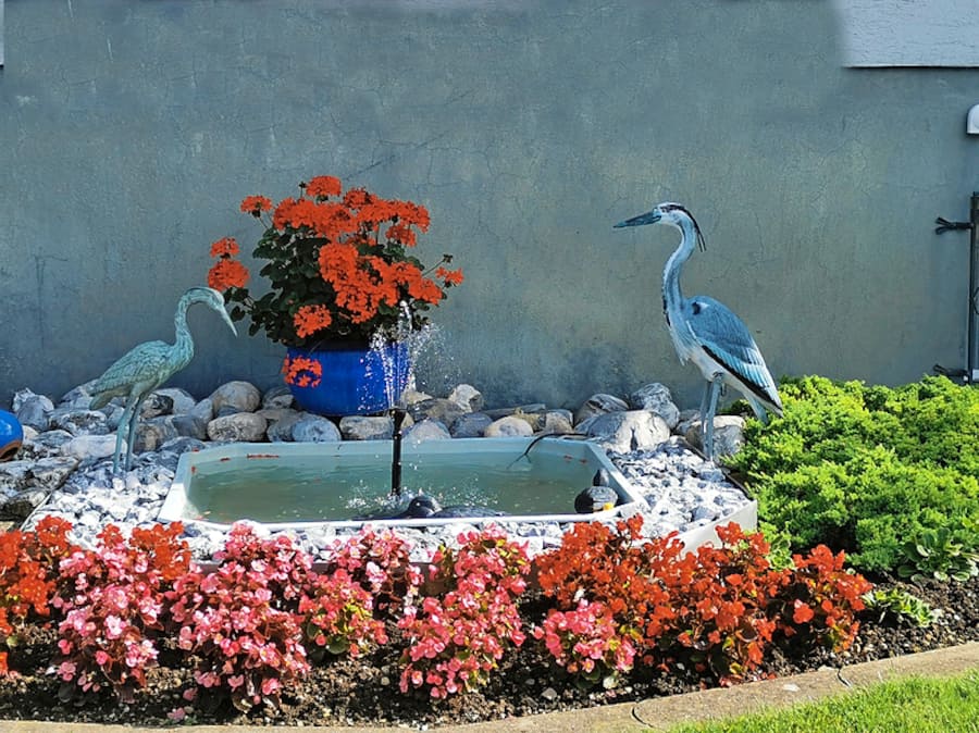 Ein Blumenbeet mit Brunnen und Reiherfiguren