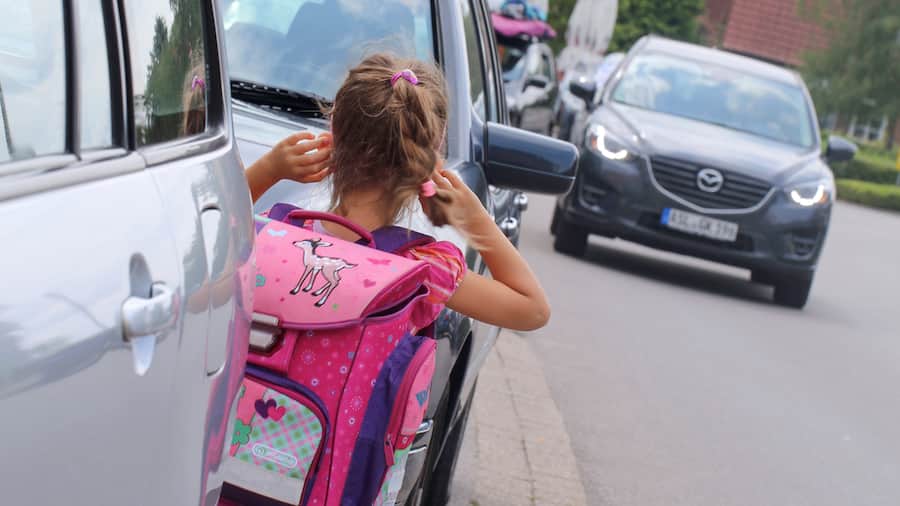 Zwischen parkierenden Autos stehende Schülerin erblickt herannahendes Auto