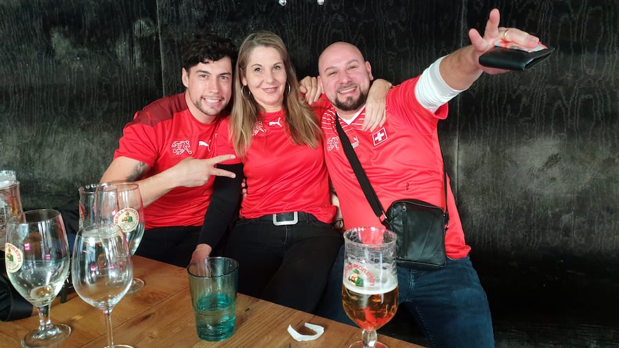 In Rot gekleidet verfolgen drei eingefleischte Fans den Spielauftakt.