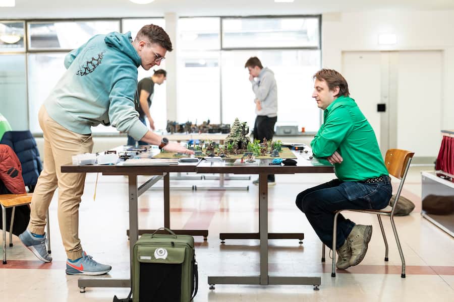 Strategisch wie Schach - mit einer Prise Zufall: Zwei Tabletopspieler an einem Tisch mit Karten, Würfeln und der künstlichen Landschaft.