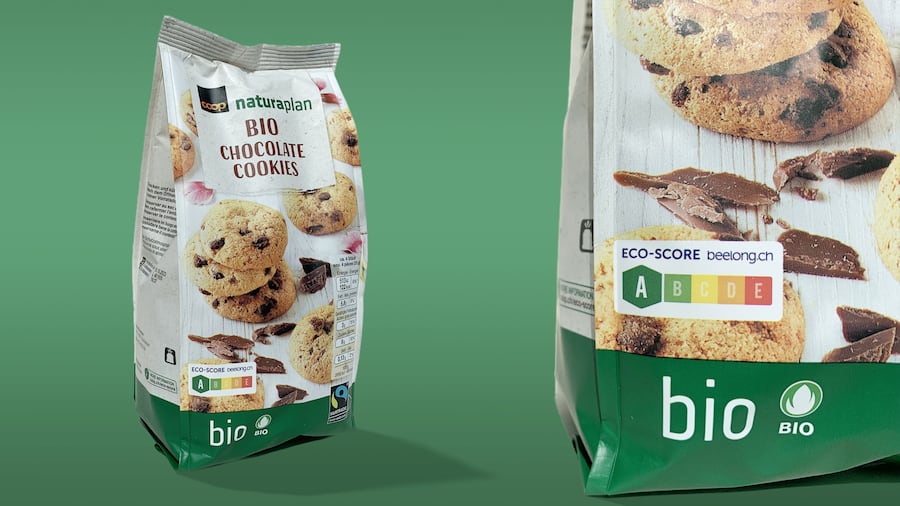 Eine Packung Bio-Schoggi-Guetsli von Coop der Eigenmarke Naturaplan steht vor einem grünen Hintergrund. Im Blickpunkt dabei die Lebensmittel-Ampel «Eco-Score», die der bekannten Nährwert-Ampel «Nutri-Score» sehr ähnlich aussieht.