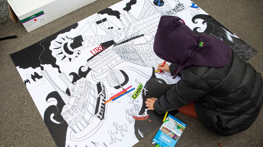 Ein Kind sitzt am Boden und zeichnet ein Bild des Paradeplatz in Zürich umgeben von Kohlebaggern und rauchenden Schornsteinen.
