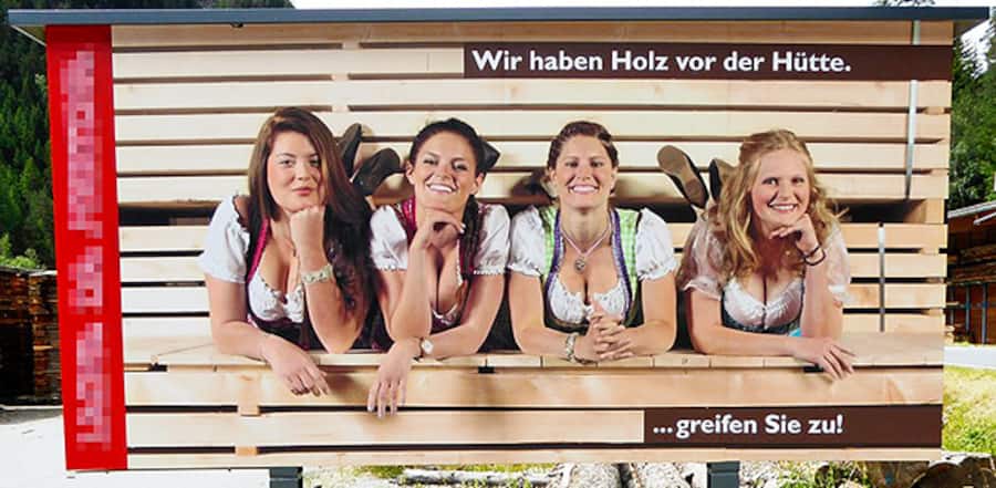 Eine Werbeplakat mit vier Frauen, die mit tiefem Décolleté vor einem Holzstapel liegen. Dazu der Spruch: «Wir haben Holz vor der Hütte. … greifen Sie zu!»