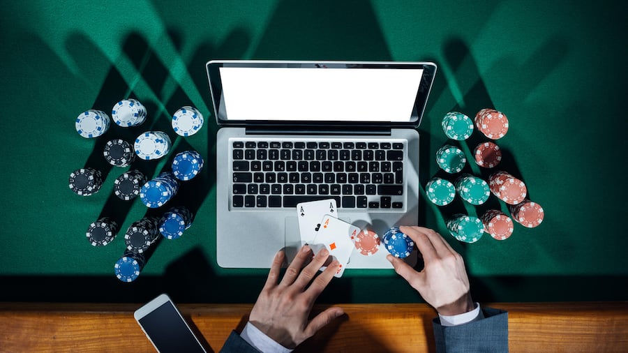 Original File ID: 290693195
Man playing online poker with laptop on a green table with chips all around, top view